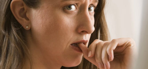 Przestraszona kobieta trzyma kciuka między zębami.