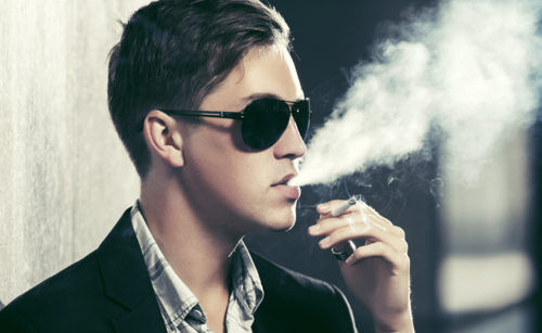 Mężczyzna w okularach przeciwsłonecznych pali papierosa.