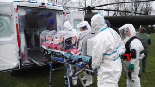 Ratownicy ubrani w kombinezony wsadzają pacjenta do ambulansu.