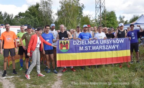 Grupa ludzi trzyma flagę dzielnicy Ursynów w Warszawie.